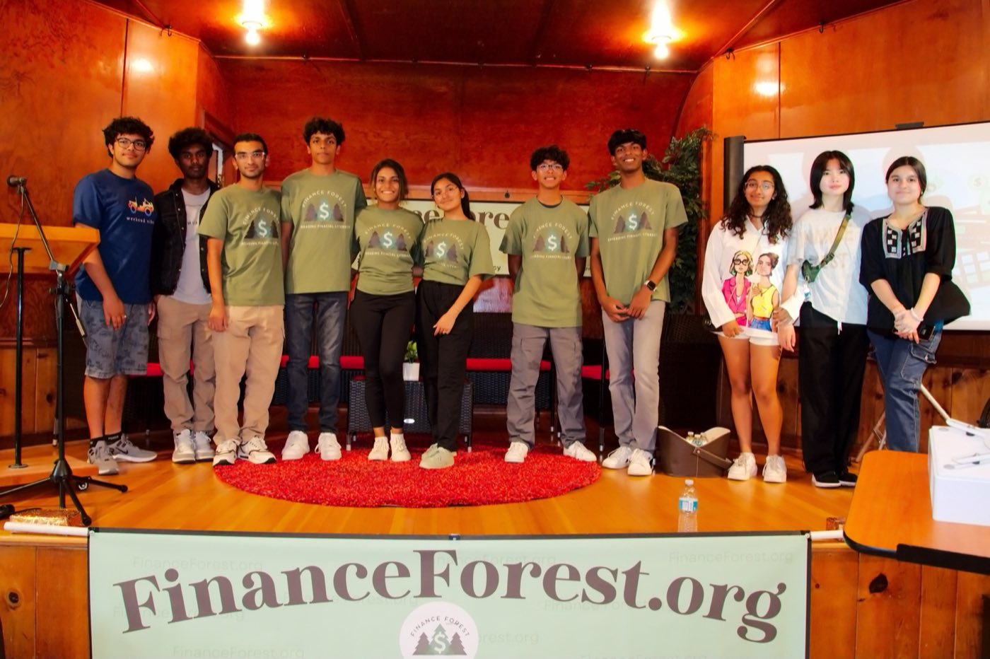 Finance Forest student volunteers on stage at a live event, behind a FinanceForest.org banner